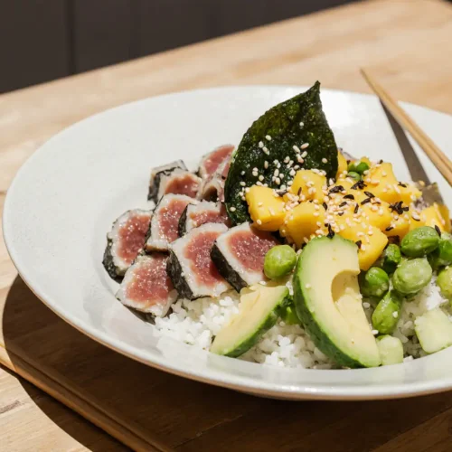 A vibrant Tuna Poke Bowl with fresh sushi-grade tuna cubes, avocado, cucumber, edamame, and sesame seeds served over rice in a ceramic bowl, captured in bright natural light.