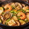 Korean seafood doenjang jjigae with shrimp, open clams, tofu and vegetables in soybean paste broth
