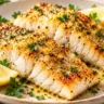Golden air fryer cod fillets with lemon pepper, parsley and lemon wedges on a ceramic plate