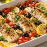 Oven-baked hake fillets with cherry tomatoes, black olives, roasted garlic, lemon and parsley in a ceramic dish